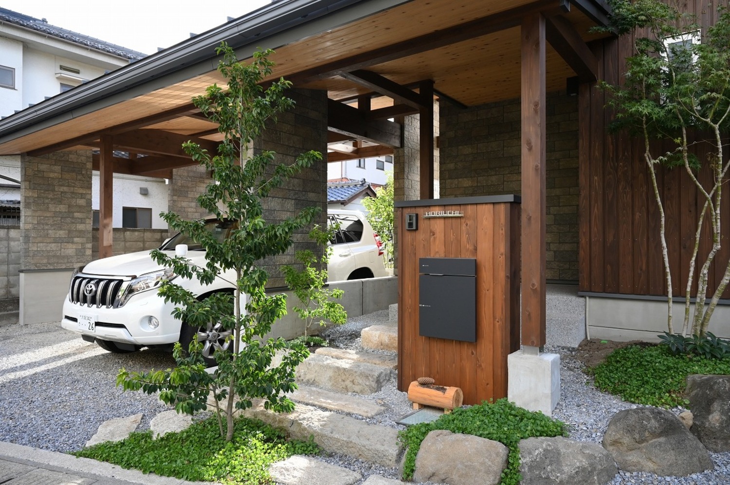 建物一体型のカーポートや石積みのアプローチ、植栽、門柱。家の顔になるからとことんこだわった。
