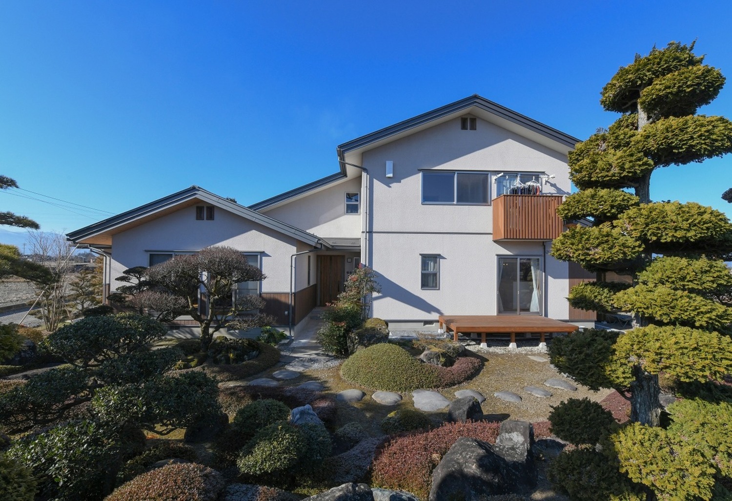 K様が大切に手入れをする庭木と調和する外観。平屋建て部分が親世帯、2階建て部分が子世帯の完全分離二世帯住宅。