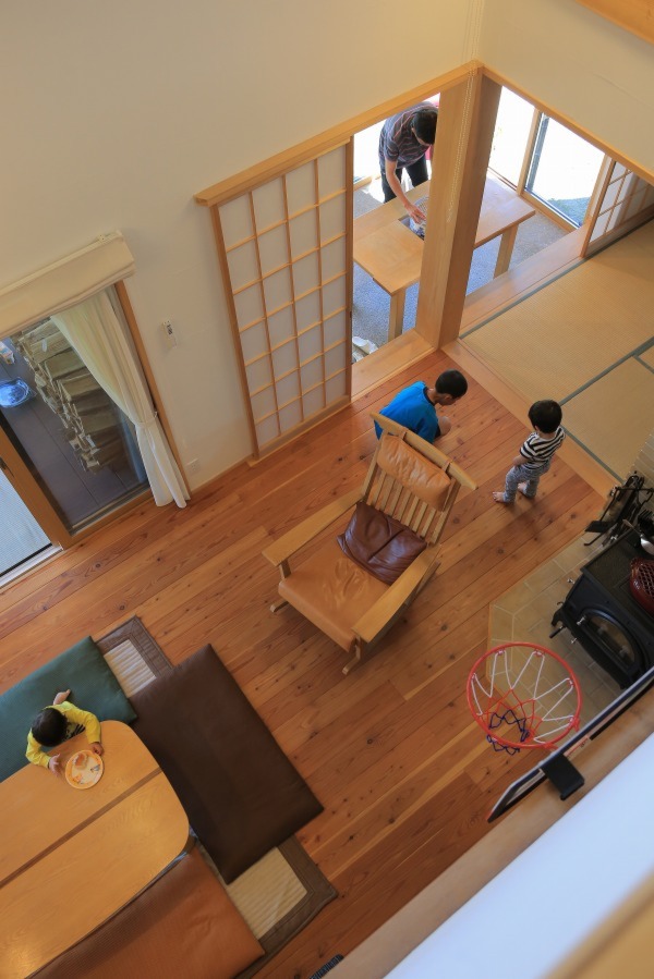 吹き抜けから見下ろすと、リビング、和室、土間サロン、ウッドデッキが連なり、2階も含めた一体空間であることが分かる。